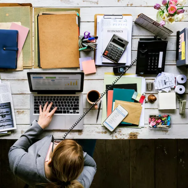 femme assise devant son ordinateur portable avec plein de document administratif à gérer