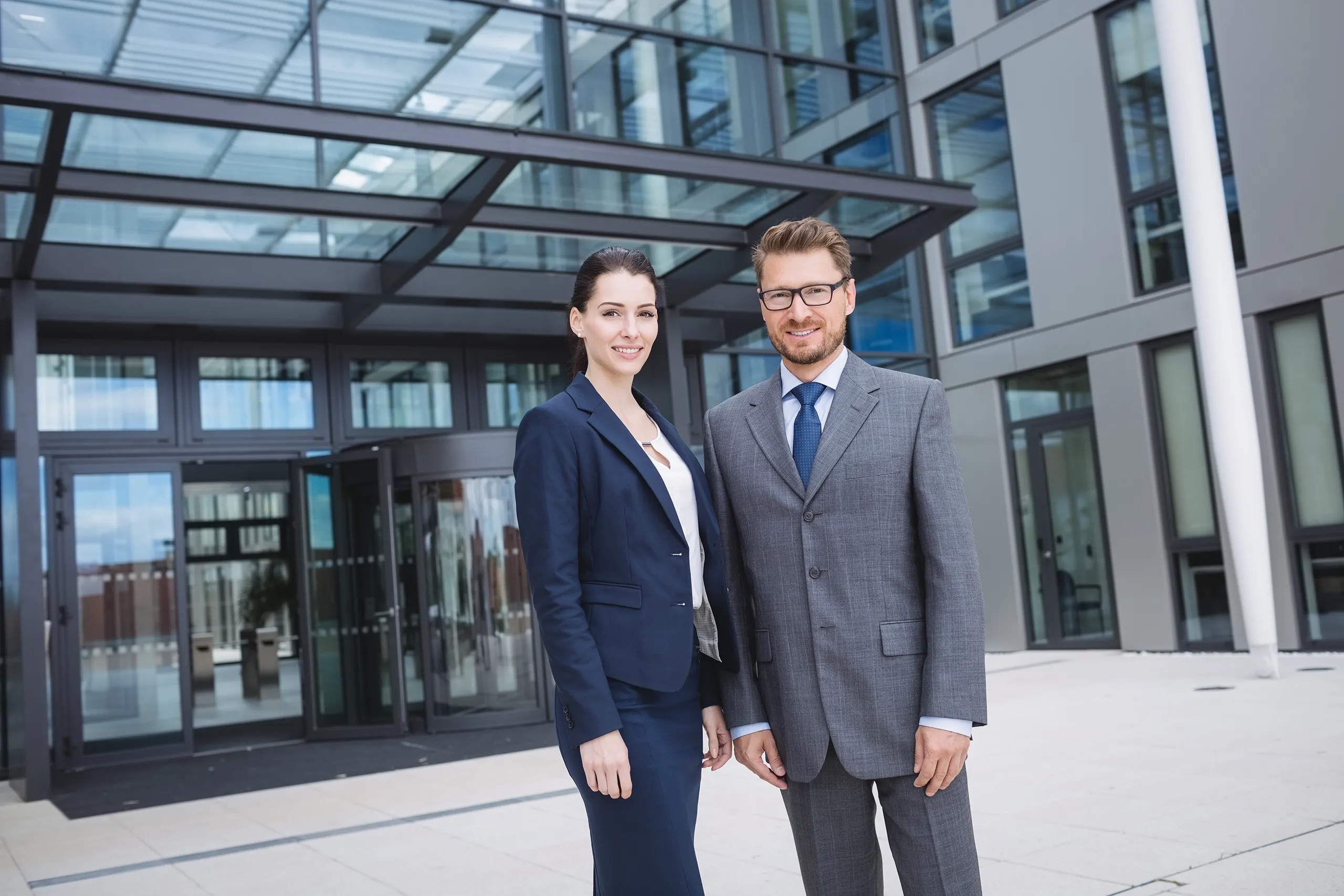 homme et femme d'affaire devant la façade vitrée d'un bureau