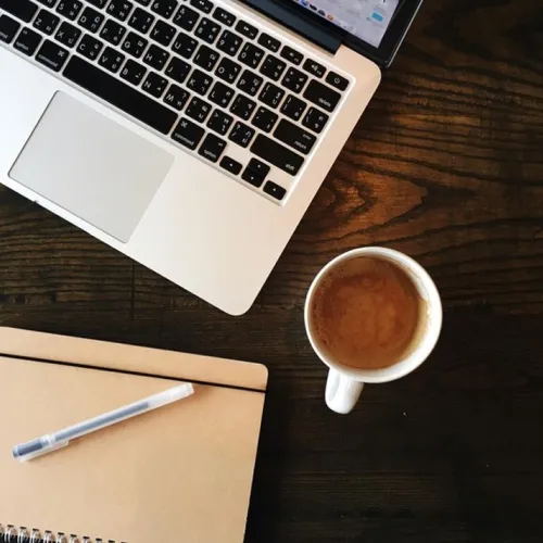 un ordinateur portable, un café et un bloc note vus de haut